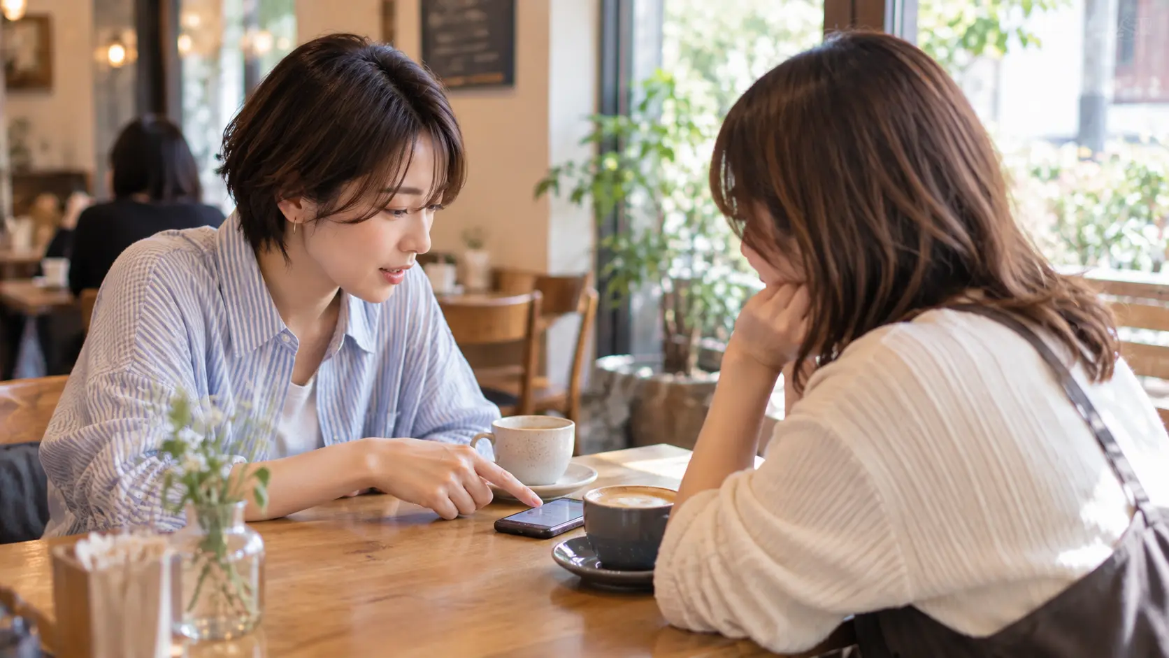 カフェでスマートフォンを前に、 写真交換や出会いについて話し合う二人の女性